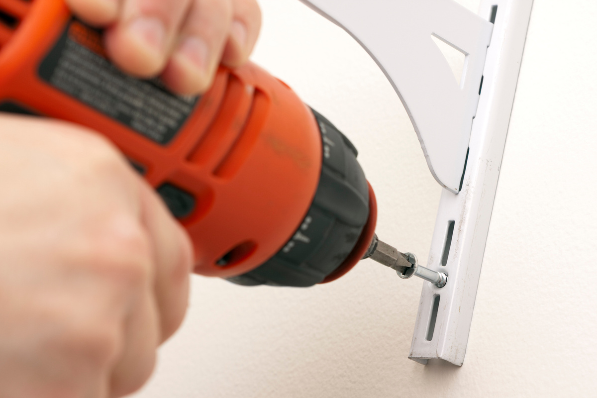 Man drilling shelves into wall